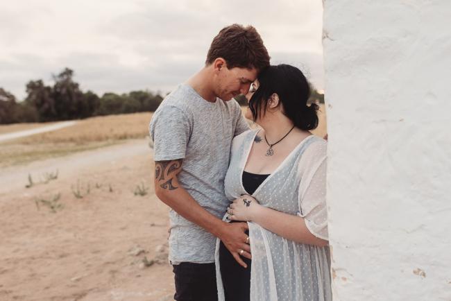 Pregnant couple forehead kissing and leaning against wall with Perth maternity photographer at Perry's Paddock