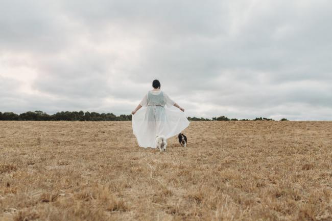 Woman walking with dogs and holding out her dress with Perth maternity photographer at Perry's Paddock