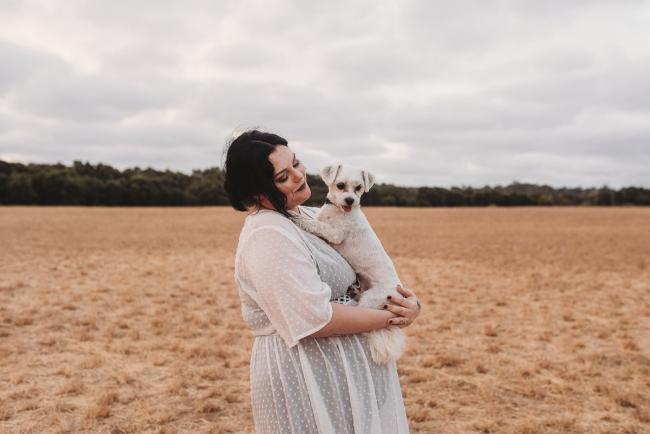 Pregnant woman holding white dog with Perth maternity photographer at Perry's Paddock