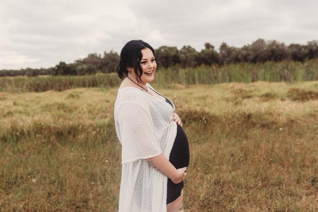 Pregnant woman smiling and holding her tummy with Perth maternity photographer at Perry's Paddock