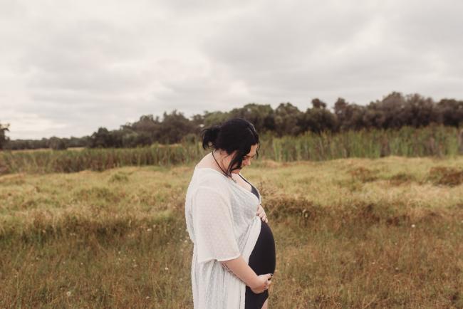 Pregnant woman holding her tummy and looking down with Perth maternity photographer at Perry's Paddock
