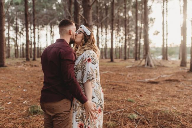 Couple holding hands and kissing at The Pines with Perth maternity photographer Alana Prosper Photography