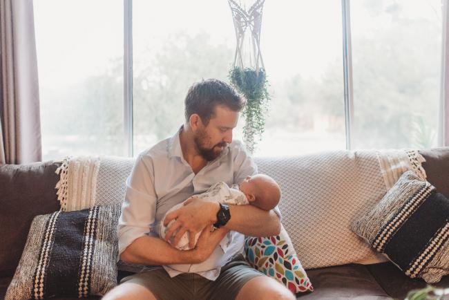 Father holding newborn baby on couch with Perth newborn lifestyle photographer Alana Prosper Photography