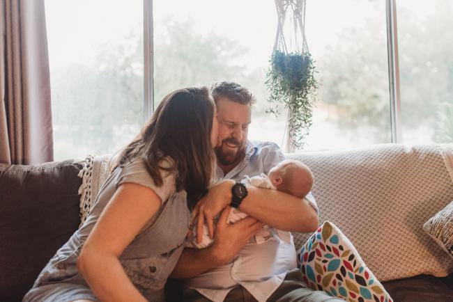 Mother kissing partner who is holding newborn baby with Perth newborn lifestyle photographer Alana Prosper Photography