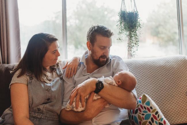 parents holding newborn baby on couch with Perth newborn lifestyle photographer Alana Prosper Photography