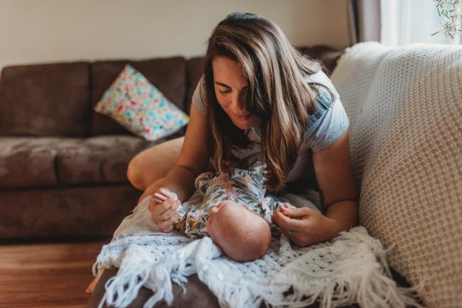 Mother leaning over to baby on couch with Perth newborn lifestyle photographer Alana Prosper Photography