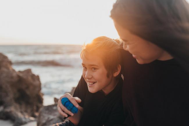 boy smiling as his mother cuddles him with Perth family photographer Alana Prosper Photography at Burns Beach