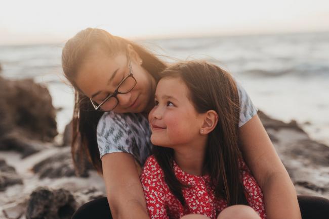 little sister looking up at big sister with Perth family photographer Alana Prosper Photography at Burns Beach