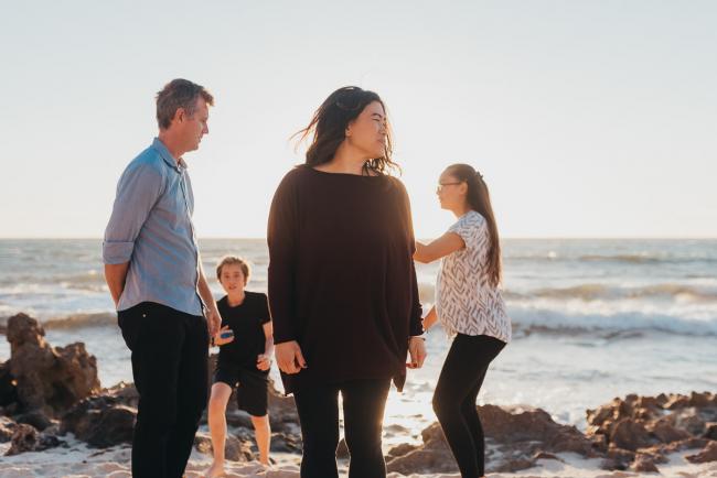 mother standing in front of family who are behind her moving around with Perth family photographer Alana Prosper Photography at Burns Beach
