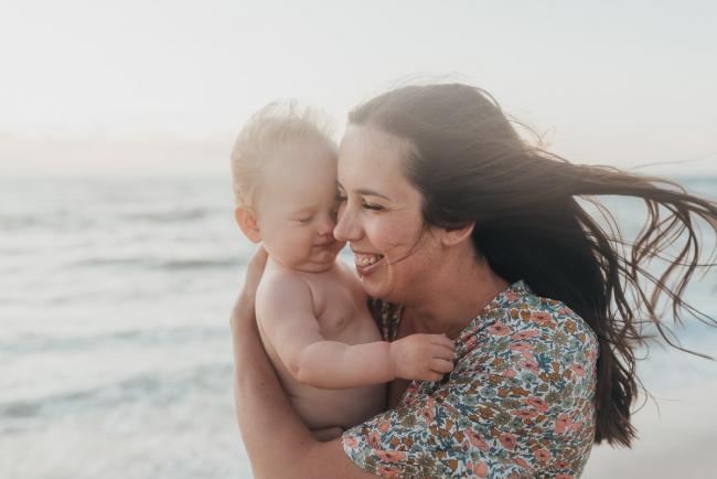 mother laughing and holding baby with family photographer Perth at Burns Beach, Alana Prosper Photography