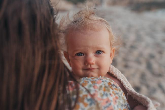 little girl looking over mothers shoulder with family photographer Perth at Burns Beach, Alana Prosper Photography