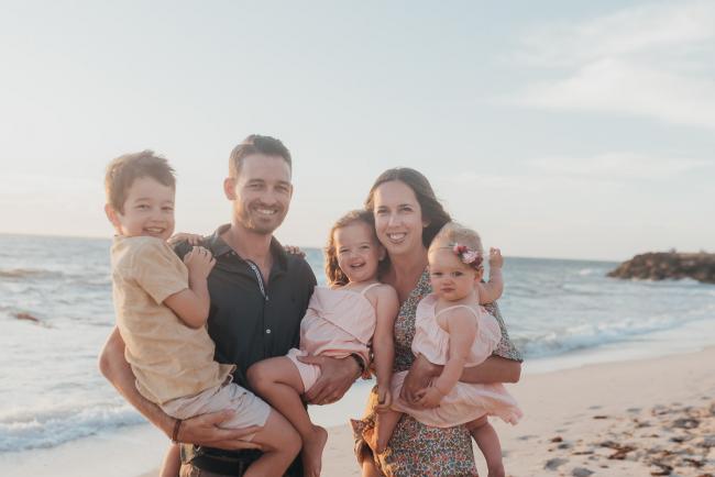 mother and father holding three kids on the beach with family photographer Perth at Burns Beach, Alana Prosper Photography