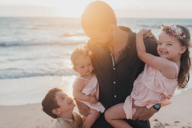 Father holding two daughters with son at his legs on the beach with family photographer Perth at Burns Beach, Alana Prosper Photography