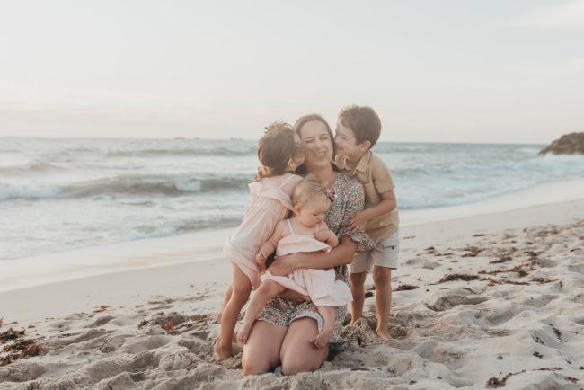 mother holding baby while two kids kiss her on the beach with family photographer Perth at Burns Beach, Alana Prosper Photography