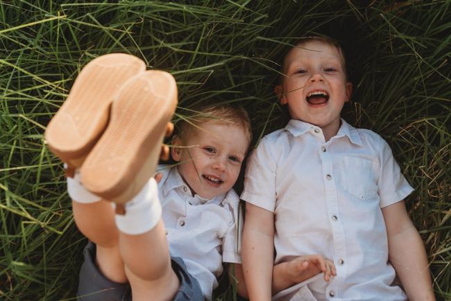 Two boys laying on the ground with one boys legs in the air during golden hour at Perry's Paddock with Perth Family Photographer Alana Prosper Photography