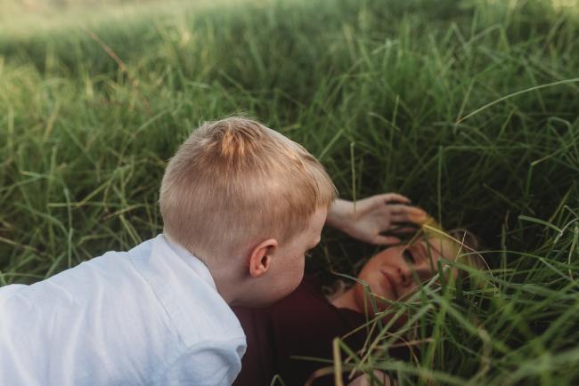 little boy laying on mother who is laying in grass during golden hour at Perry's Paddock with Perth Family Photographer Alana Prosper Photography