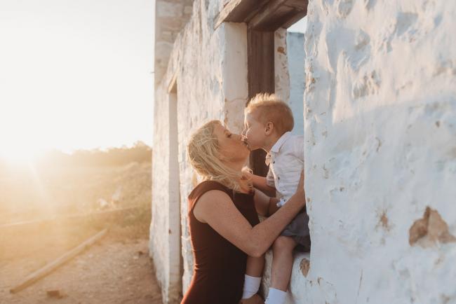 boy sitting in window frame of white house kissing mother during golden hour at Perry's Paddock with Perth Family Photographer Alana Prosper Photography