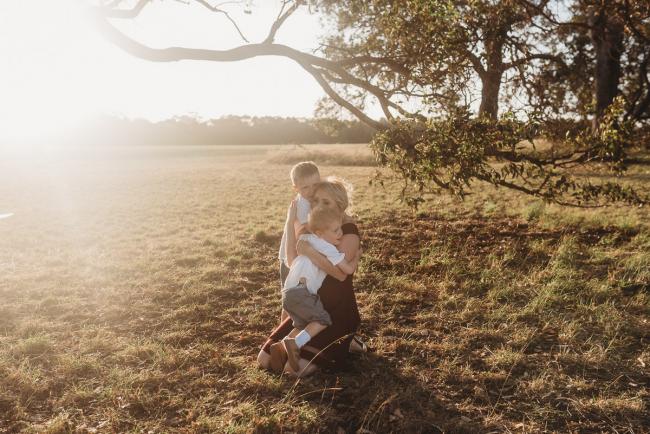 Two sons cuddling mother kneeling on the ground during golden hour at Perry's Paddock with Perth Family Photographer Alana Prosper Photography