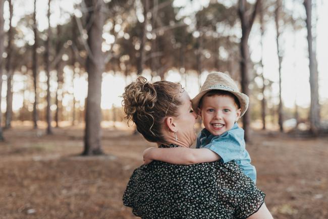 mother carrying little boy smiling over her shoulder during Perth family photography session at The Pines Perth with Alana Prosper Photography