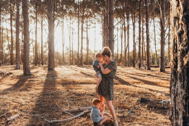 Mother holding one son while the other son hugs her legs during Perth family photography session at The Pines Wanneroo