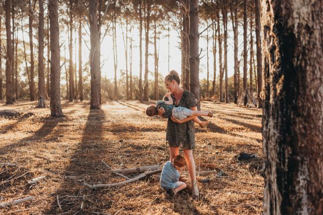 Mother holding one son while the other son hugs her legs during Perth family photography session at The Pines Wanneroo