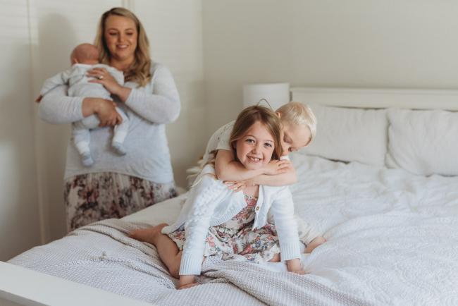 Perth-Newborn-Photographer-Alana-Prosper-Photography-11-of-31 brother on sisters back with mother and baby in background with Perth lifestyle newborn photographer Alana Prosper Photography