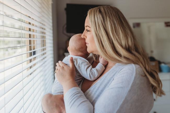 mother standing in front of window with baby with Perth lifestyle newborn photographer Alana Prosper Photography