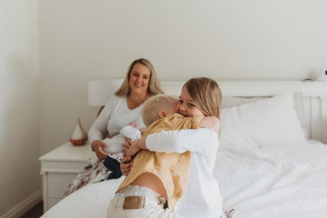 Perth-Newborn-Photographer-Alana-Prosper-Photography-5-of-31 brother and sister hugging with mother and baby in background with Perth lifestyle newborn photographer Alana Prosper Photography