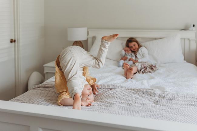Perth-Newborn-Photographer-Alana-Prosper-Photography-8-of-31 little girl holding baby brother on bed with other brother doing roly poly with Perth lifestyle newborn photographer Alana Prosper Photography