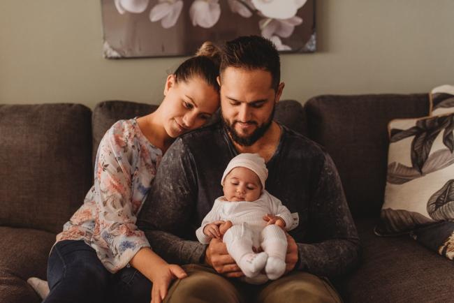 Father holding newborn baby on lap as mother leans on his shoulder with Perth newborn lifestyle photographer