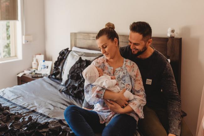 Parents holding newborn baby on bed with Perth newborn lifestyle photographer