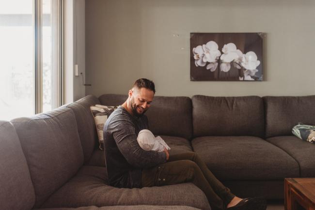 father sitting on couch with newborn baby with Perth newborn lifestyle photographer