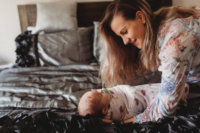 Mother picking baby up from bed with Perth newborn lifestyle photographer