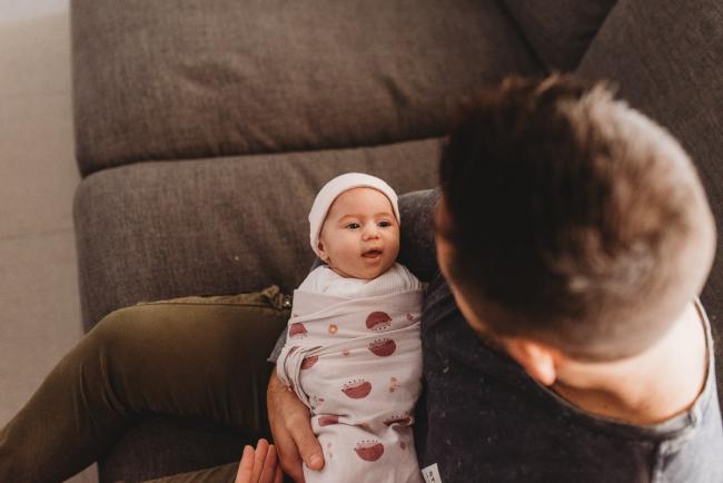 Baby wrapped and smiling up at father who is holding her with Perth newborn lifestyle photographer