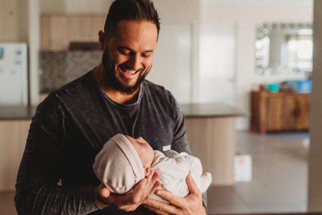 Father smiling down at baby in his arms with Perth newborn lifestyle photographer