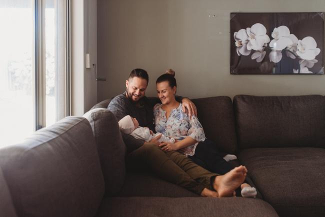 Mother and father holding newborn baby on couch with Perth newborn lifestyle photographer