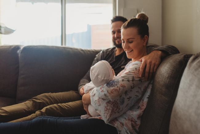 Mother and father holding newborn baby on couch with Perth newborn lifestyle photographer