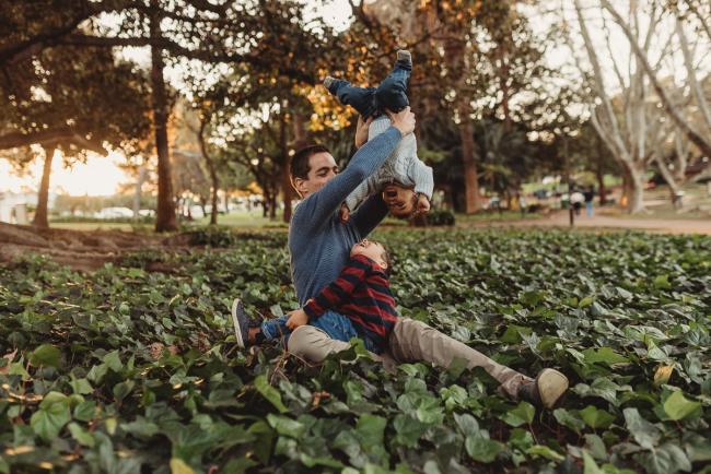 father lifting son upside down with other son on his lap with Perth family photographer Alana Prosper Photography at Hyde Park