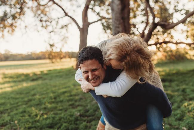 husband giving wife piggyback with Perth family photographer Alana Prosper Photography at Perry's Paddock