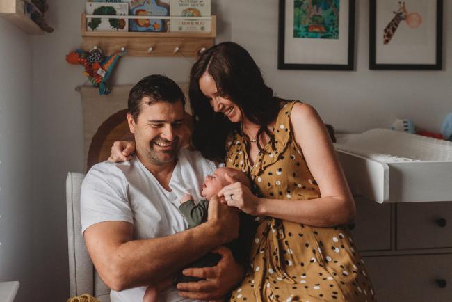 mother and father sit in chair with baby with Perth Newborn photographer