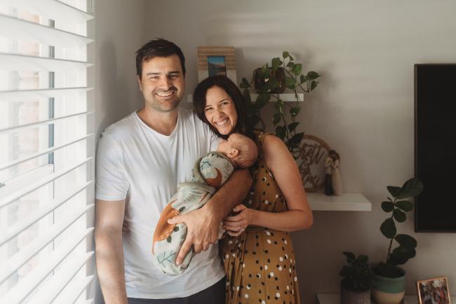 mother and father stand by window with baby with Perth Newborn photographer