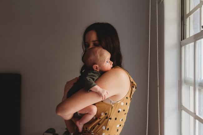 mother holding baby over her shoulder by window with Newborn photographer Perth