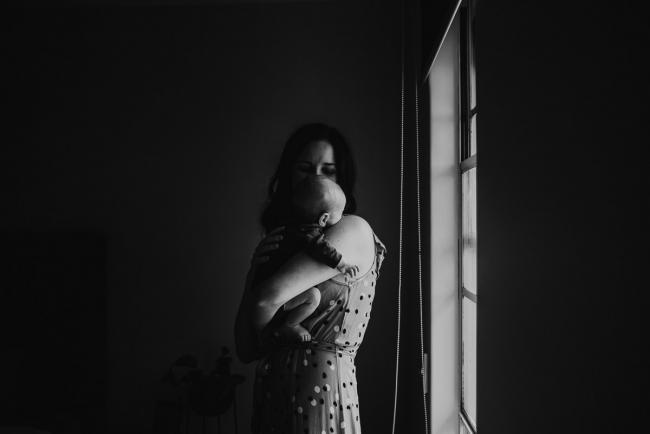 black and white image of mother holding baby over shoulder by window with Perth Newborn photographer