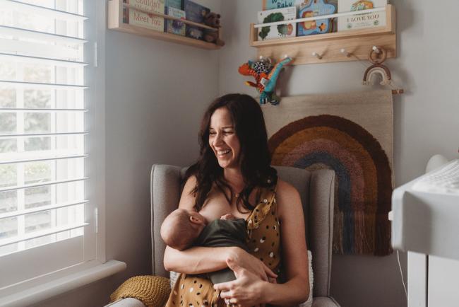 mother laughing while breastfeeding in chair with Perth Newborn photographer