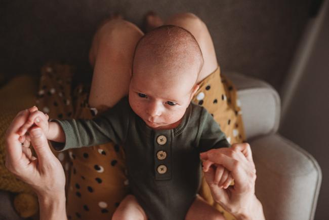 mother holding hands of baby as baby lays in her lap with Perth Newborn photographer