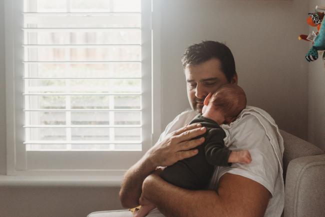 father holds baby on shoulder by window with Perth Newborn photographer